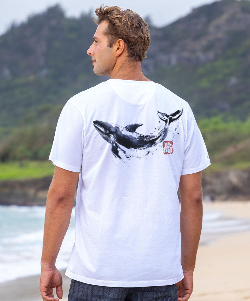 Man in a white t-shirt with a whale design on the back, standing on a beach View 2