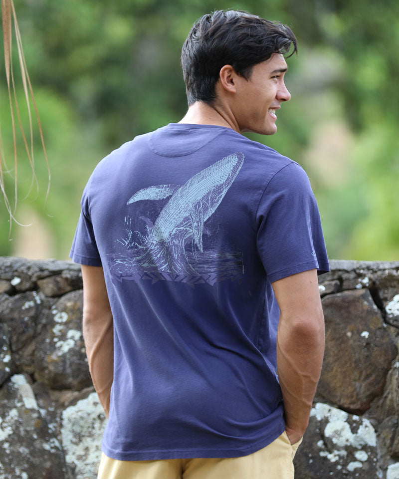 Man wearing a indigo t-shirt with a graphic design, standing outdoors against a stone wall. View 2