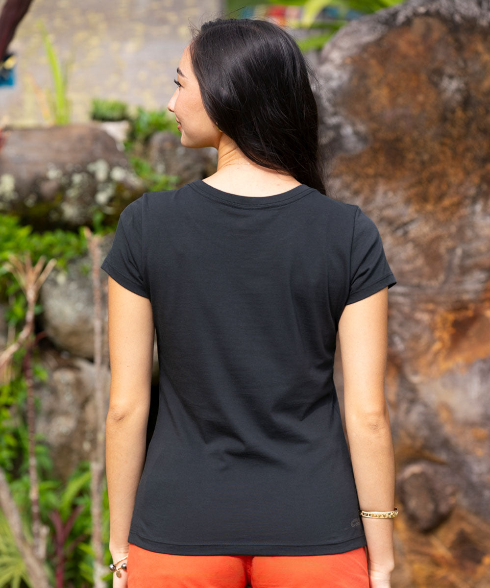 Woman wearing a black t-shirt with a natural stone wall and greenery in the background View 3