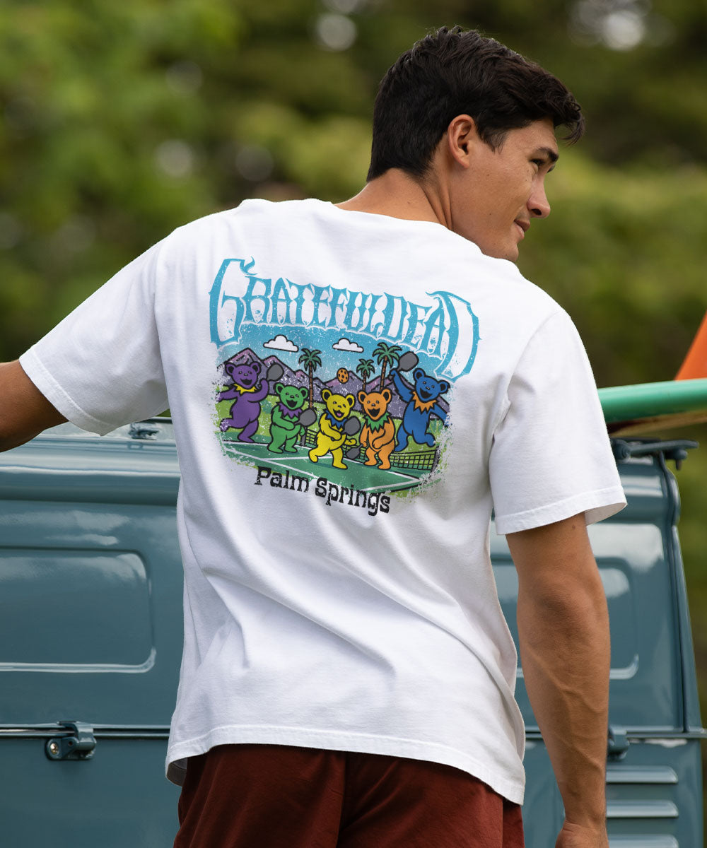 Man wearing a white t-shirt with a colorful graphic design, standing next to a vintage truck. View 2