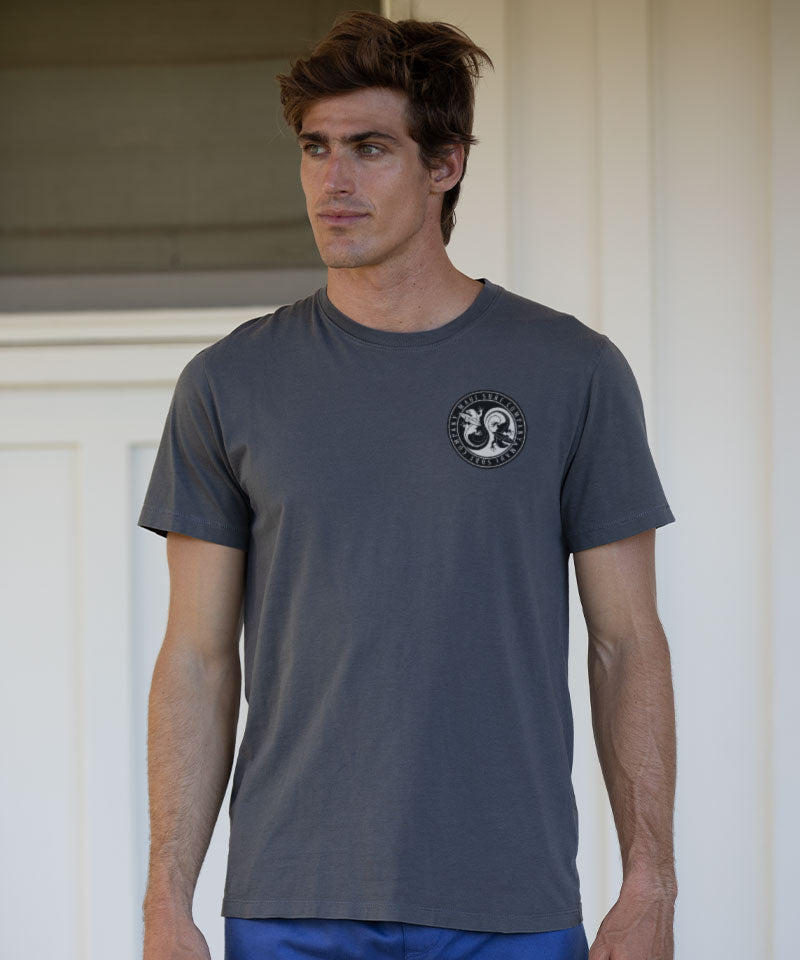 Man wearing a grey t-shirt with a small logo standing outside View 3
