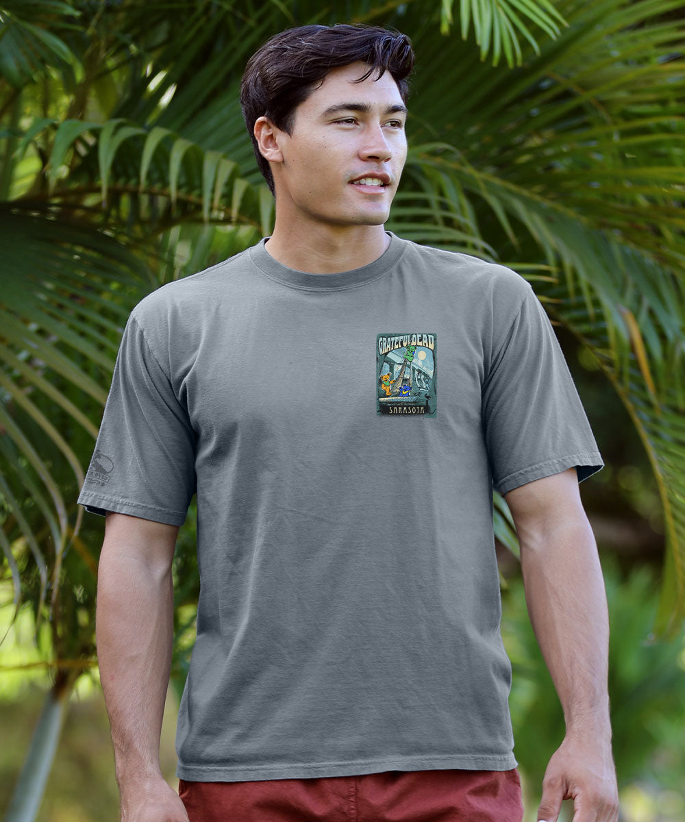 Man wearing a gray t-shirt with a small logo standing in front of trees View 3