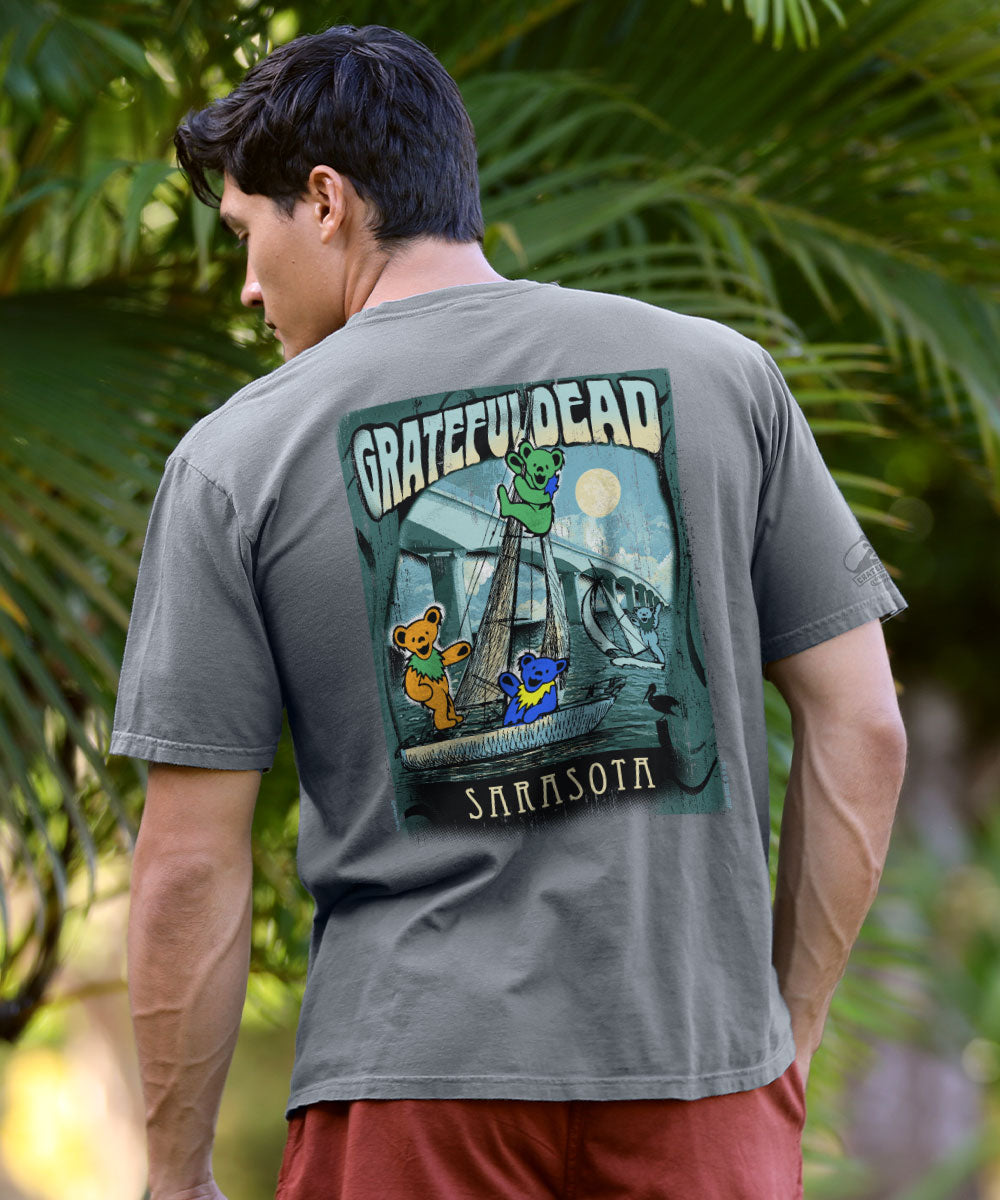 Man wearing a gray t-shirt with a graphic on the back, standing against plants View 2