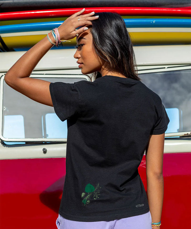 Woman wearing a black t-shirt with a logo in front of a colorful vehicle. View 3