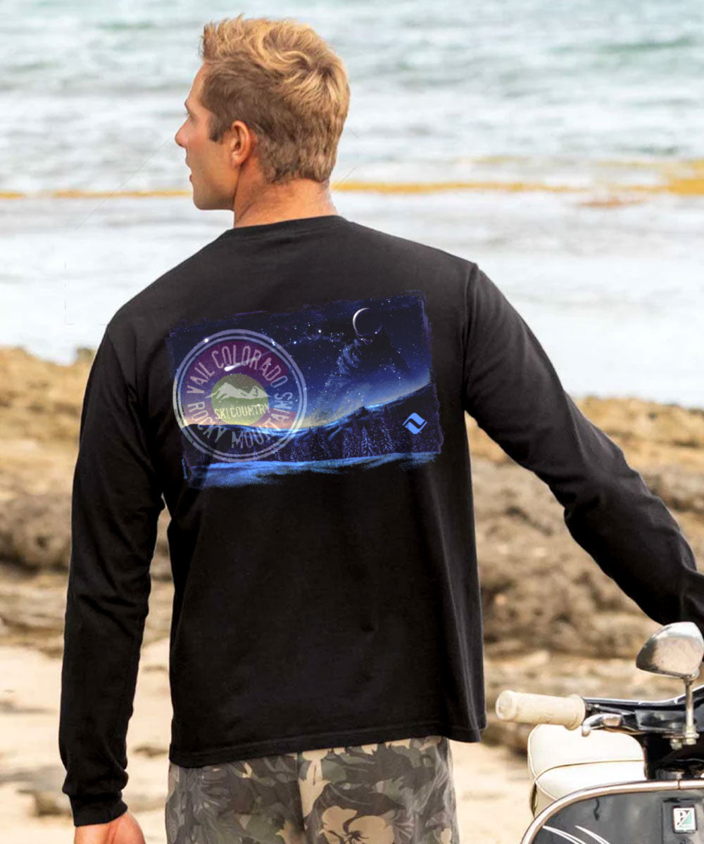 Person wearing a black long-sleeve shirt with a graphic design on the back, standing by a body of water. View 2