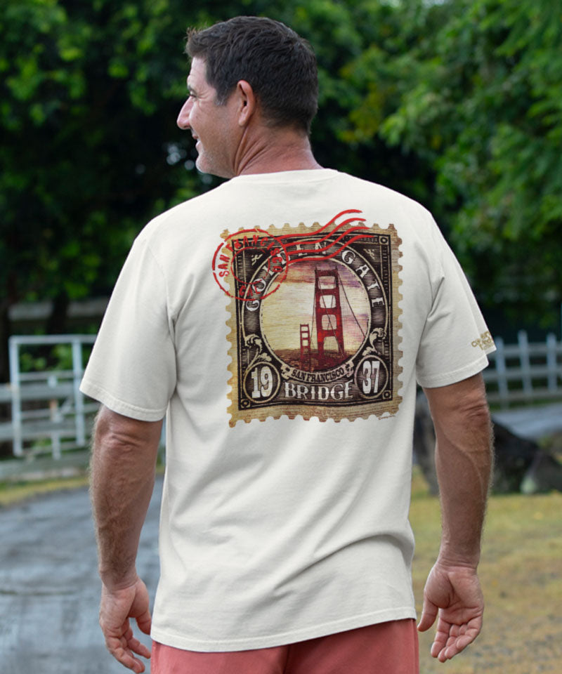 Man wearing creamy white a t-shirt with a Golden Gate Bridge design on the back, standing outdoors. View 2
