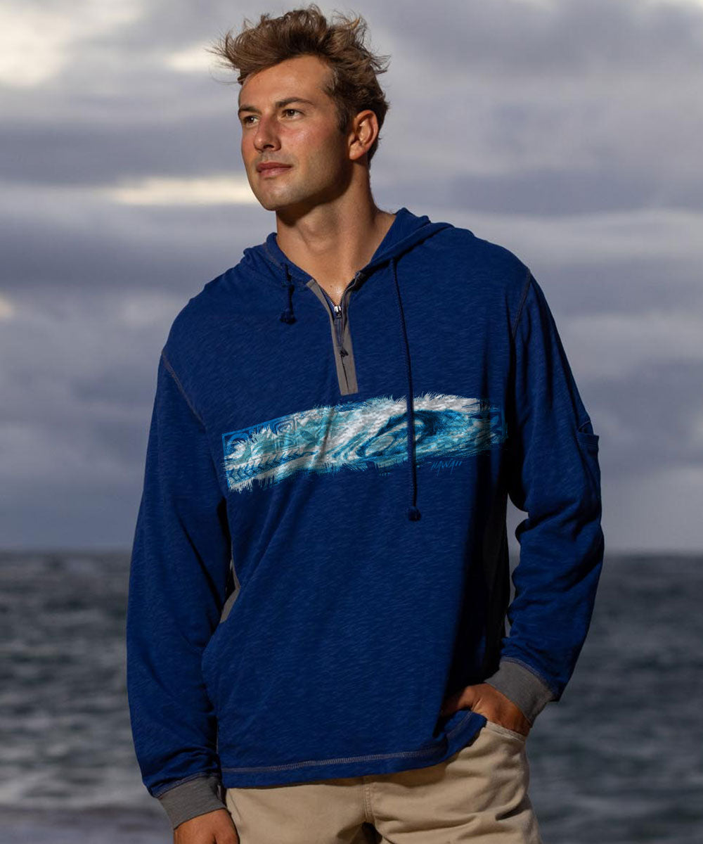 Man wearing a blue hoodie with a wave design, standing against a cloudy sky and ocean. View 2