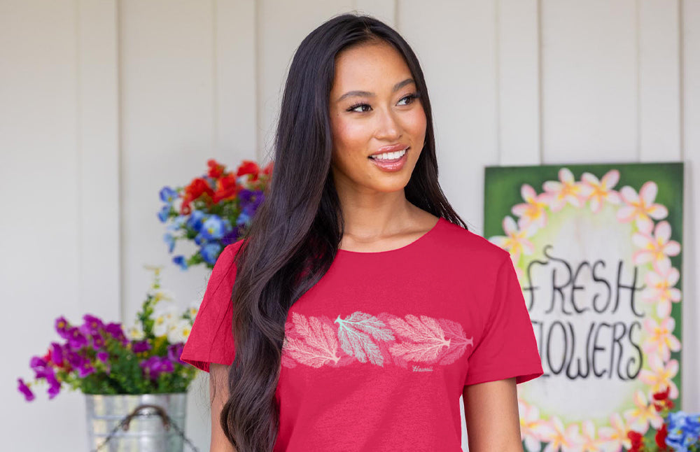 Woman wearing a red t-shirt with floral design in an outdoor setting with flowers and a sign in the background.