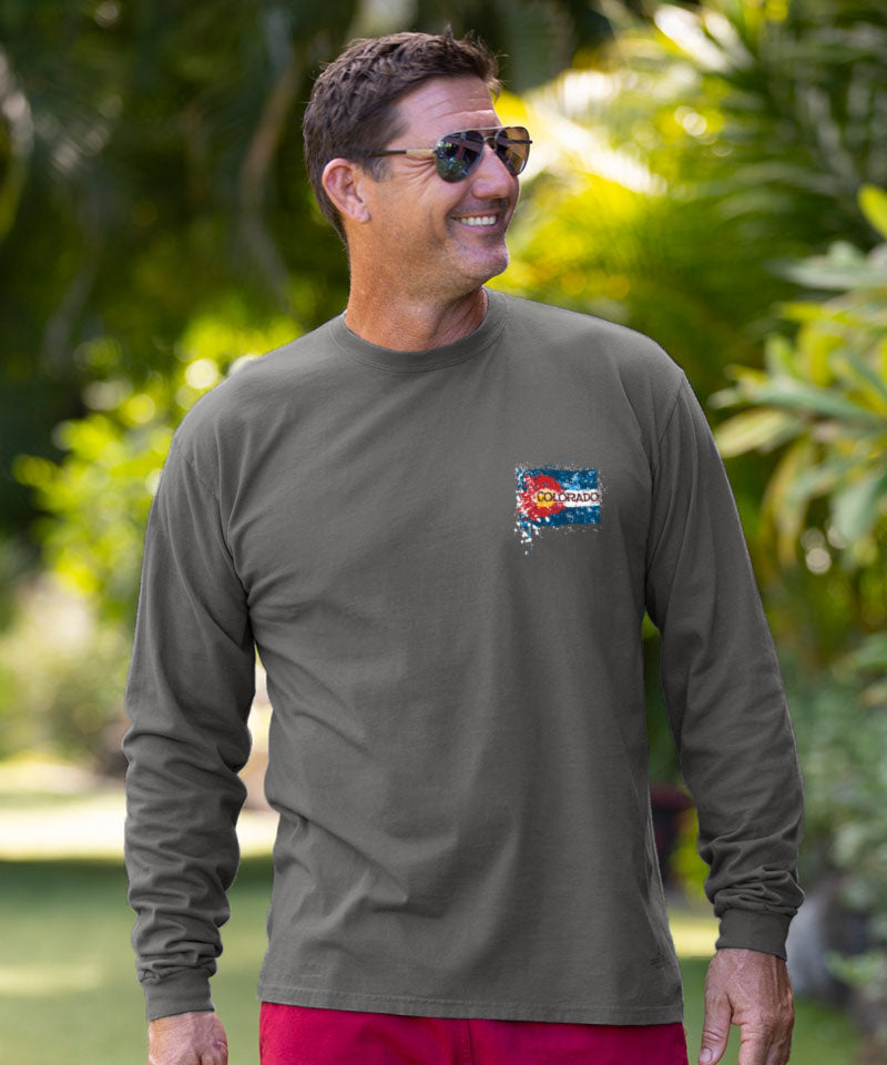 Man wearing a green long-sleeve shirt with a logo, standing outdoors with greenery in the background. View 3
