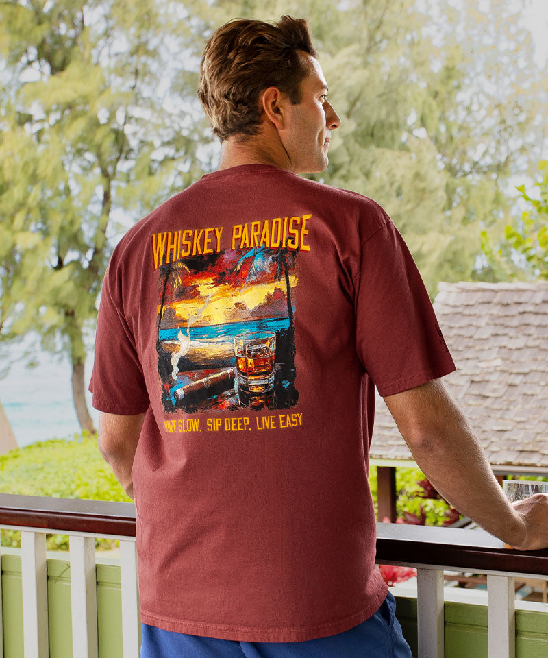 Man wearing a 'Whiskey Paradise' t-shirt on a balcony with greenery in the background