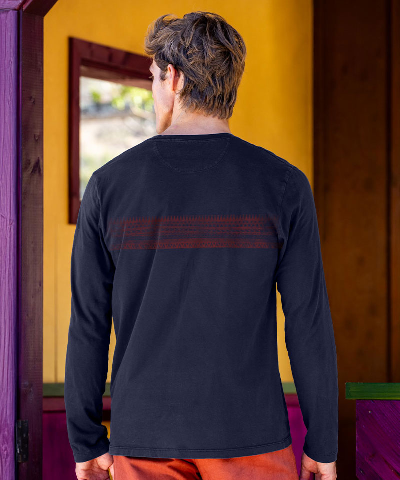 Person wearing a black long-sleeve shirt with text on the back, standing in front of a yellow wall. View 3