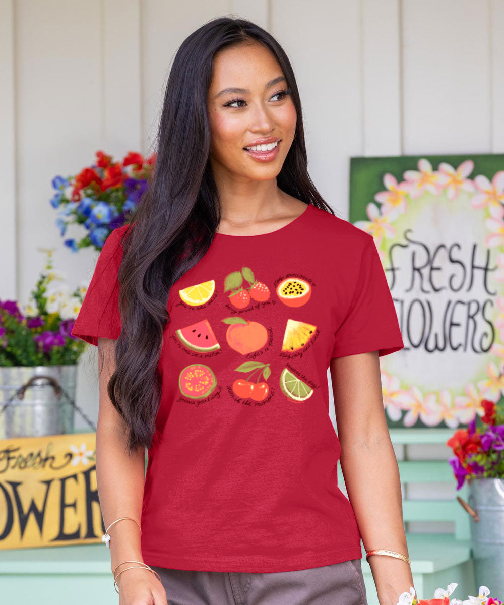 Woman wearing a raspberry dyed  t-shirt with fruit graphics in an outdoor setting with flowers and signs.