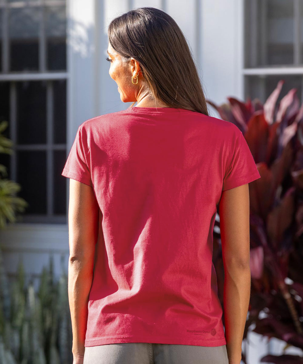 Person wearing a raspberry dyed t-shirt with a logo on the back, standing outdoors. View 3