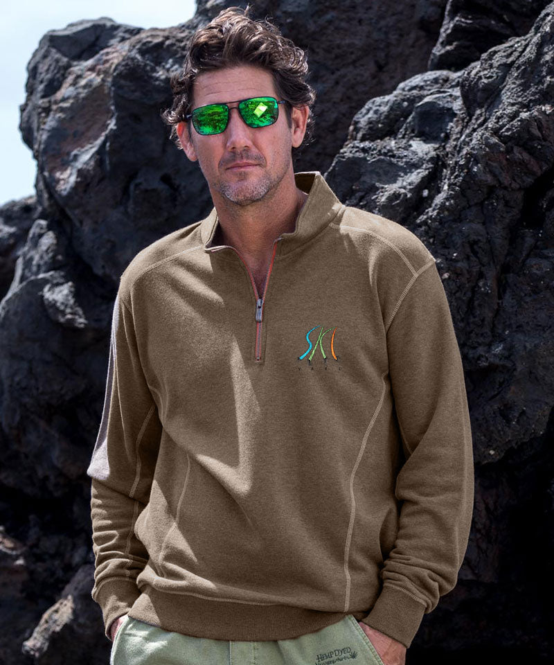 Man wearing a brown pullover with a logo, standing against dark rocks. View 2