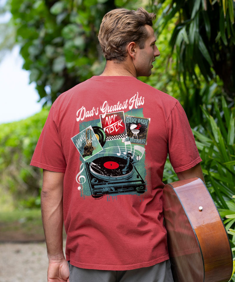 Man wearing a red t-shirt with a graphic design, holding a guitar outdoors. View 2