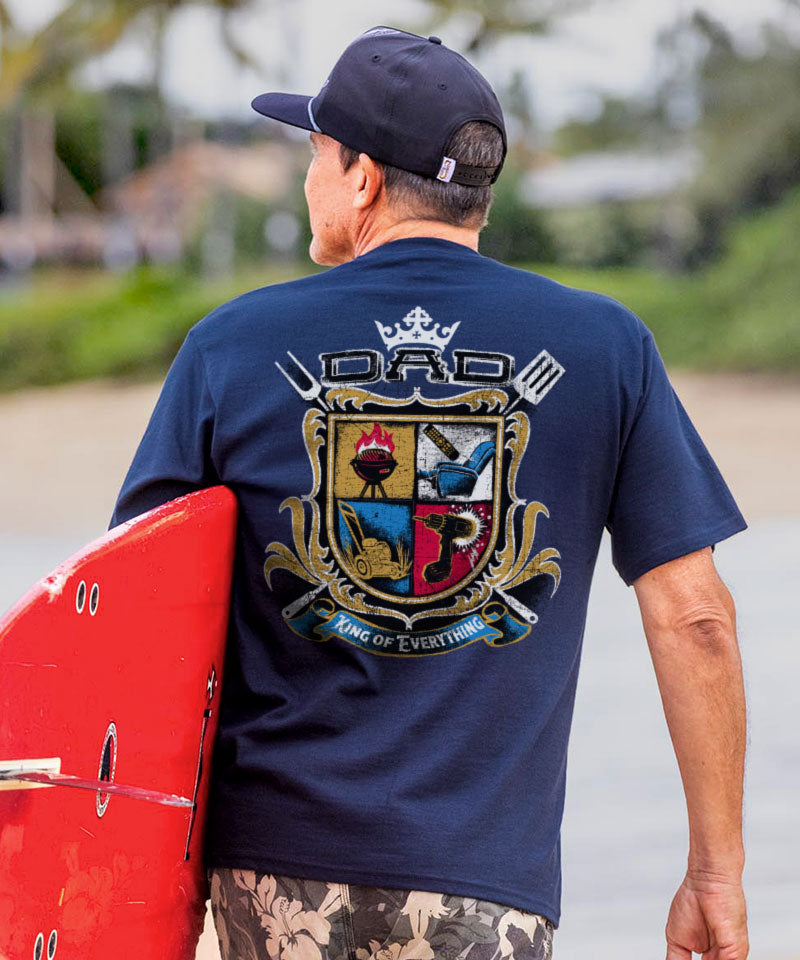 Man wearing a blue t-shirt with a colorful crest design, holding a red surfboard. View 2