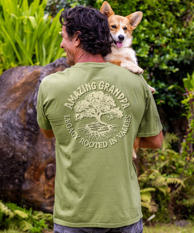 Man wearing a green t-shirt with 'Amazing Grandpa' text and a dog on his shoulders in a natural setting.
