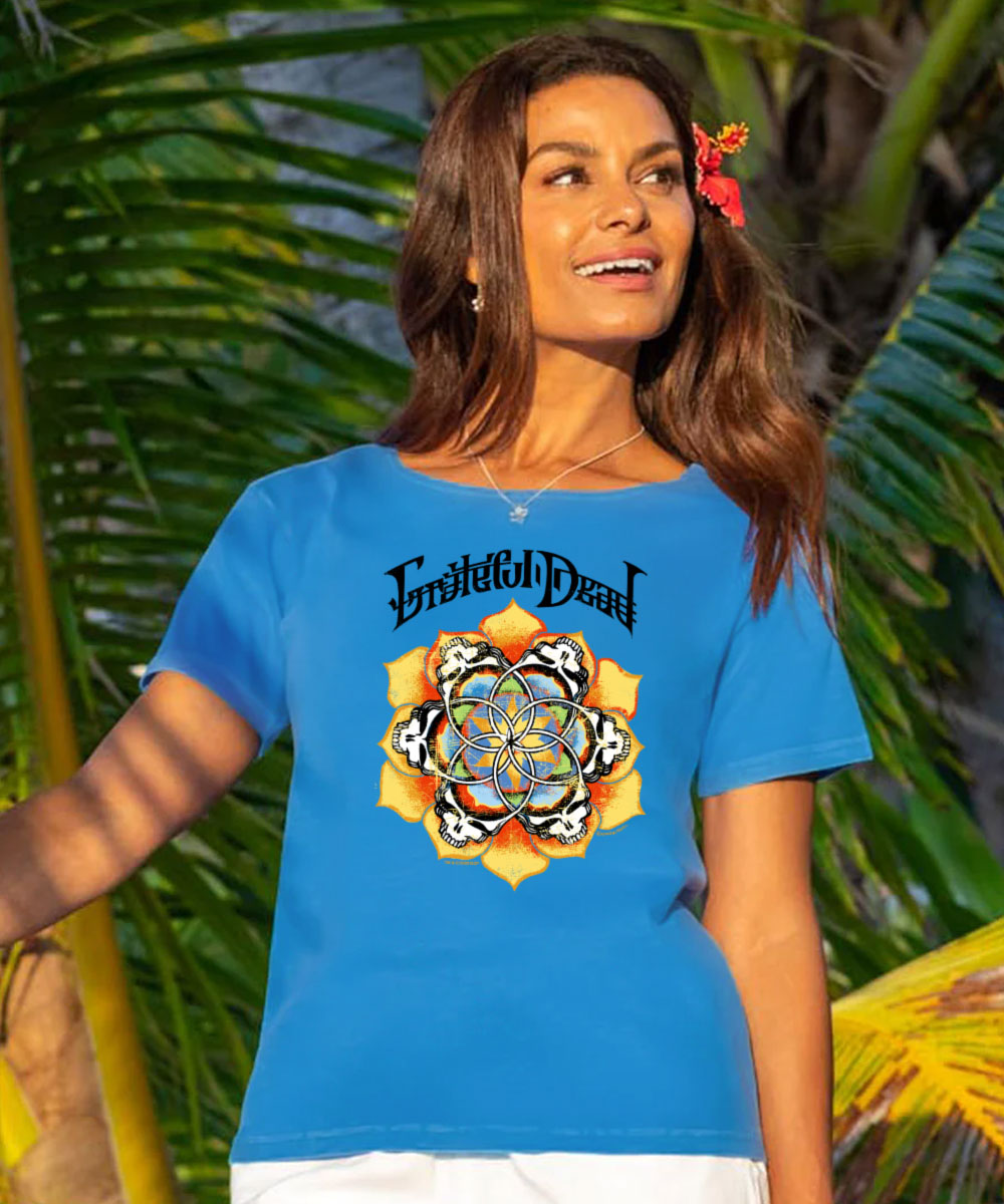 A woman wearing a bright blue t-shirt with a colorful graphic of the band 'Eternal Dead' and a mandala design, set against a tropical background of palm leaves. View 2