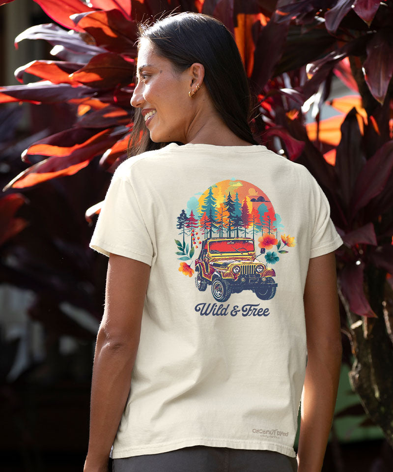 Woman wearing a t-shirt with a colorful graphic design of a Jeep and nature elements, standing in front of leafy plants. View 2