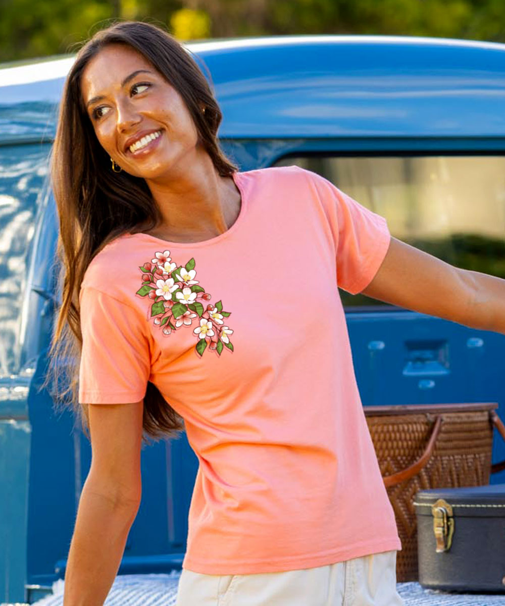 Woman wearing a pink t-shirt with a floral design, standing next to a blue truck. View 2