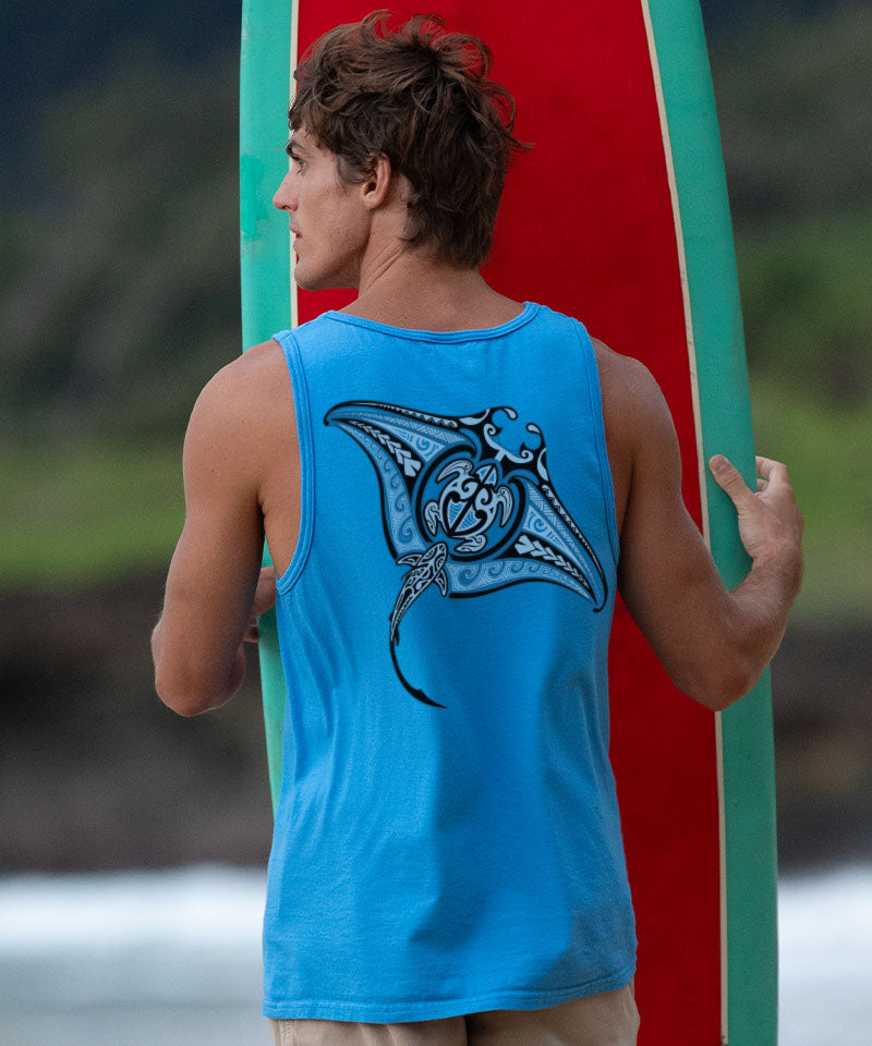 Man wearing a blue tank top with a shark design on the back standing on the beach. View 2