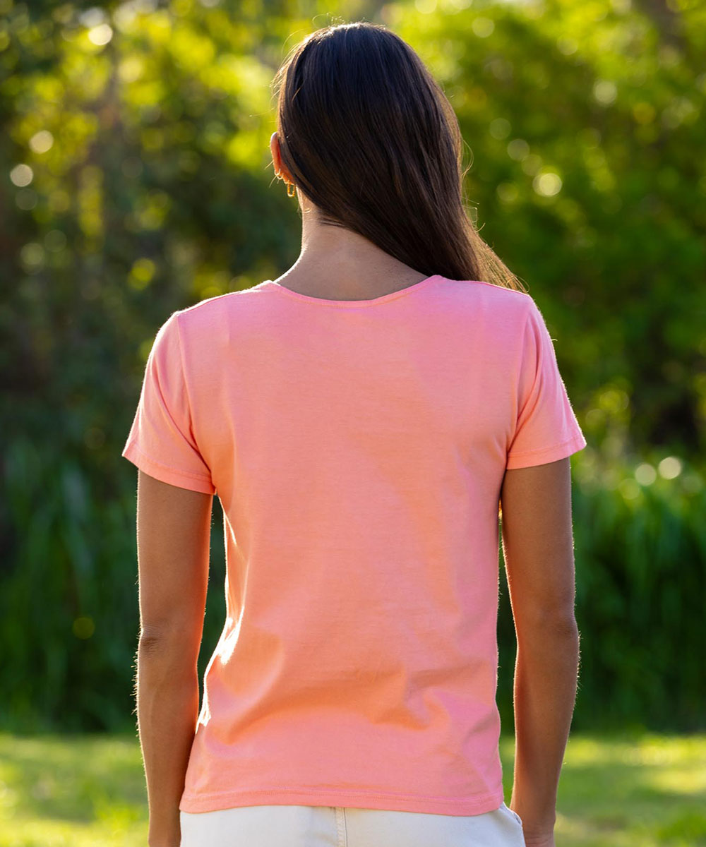 Person wearing a coral t-shirt standing outdoors with greenery in the background View 3