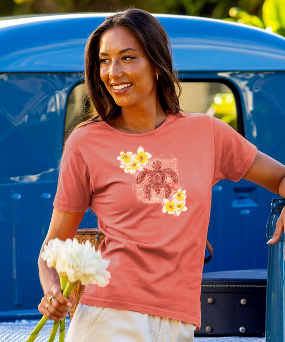 Woman in a coral t-shirt with a graphic design, holding flowers, standing next to a blue truck. View 2