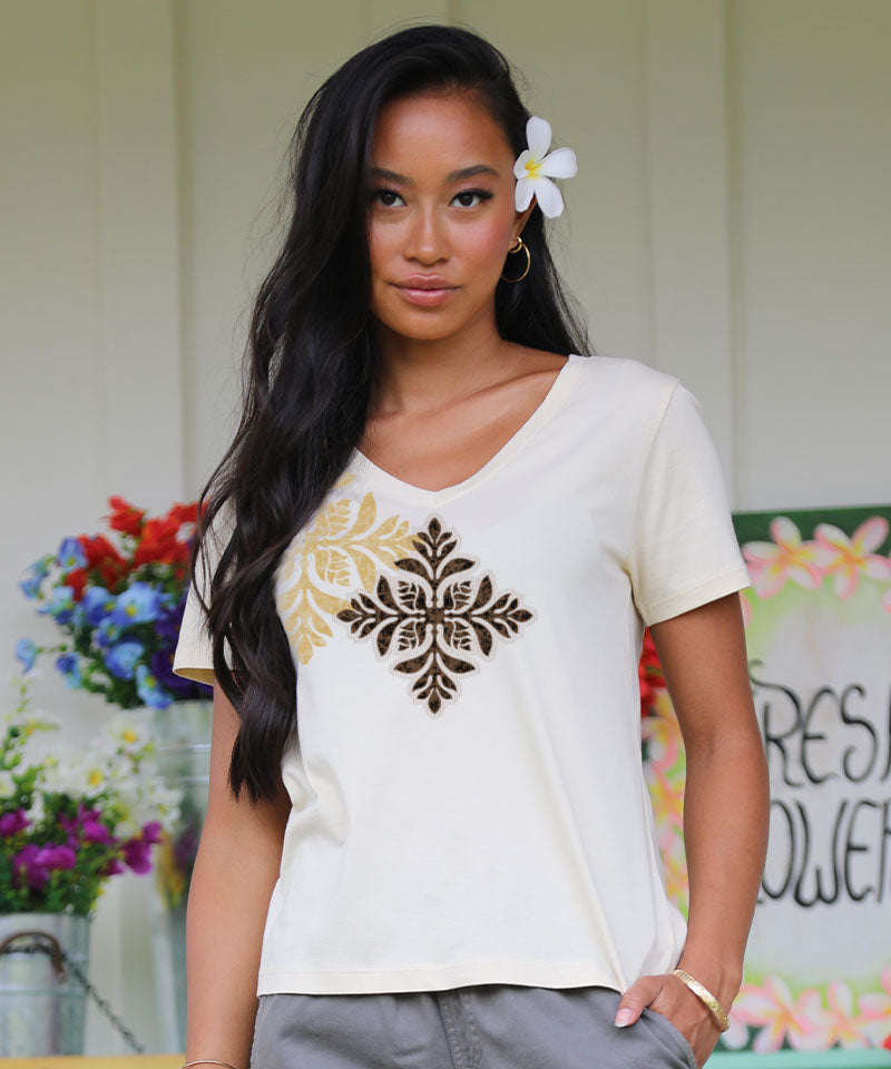 Woman wearing a white t-shirt with a decorative design, standing outdoors with flowers and a sign in the background. View 2