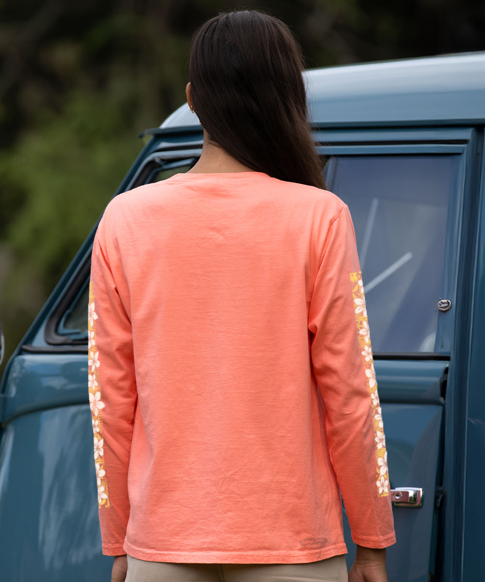 Person wearing a coral long-sleeve shirt with floral designs in front of a blue car. View 3