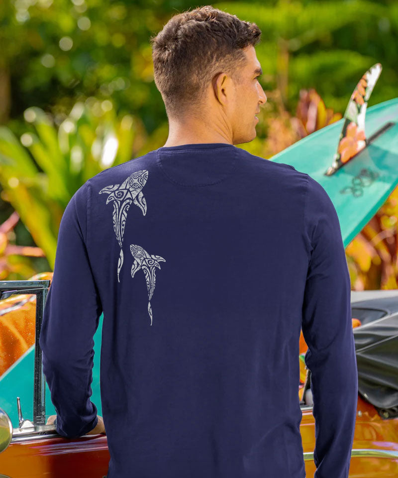 Man wearing a navy long-sleeve shirt with shark designs, standing next to a kayak. View 3