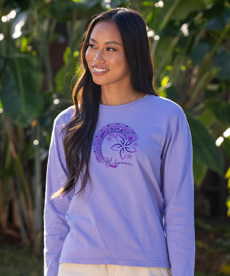 Woman wearing a purple long-sleeve shirt with a logo, standing outdoors with greenery in the background. View 2