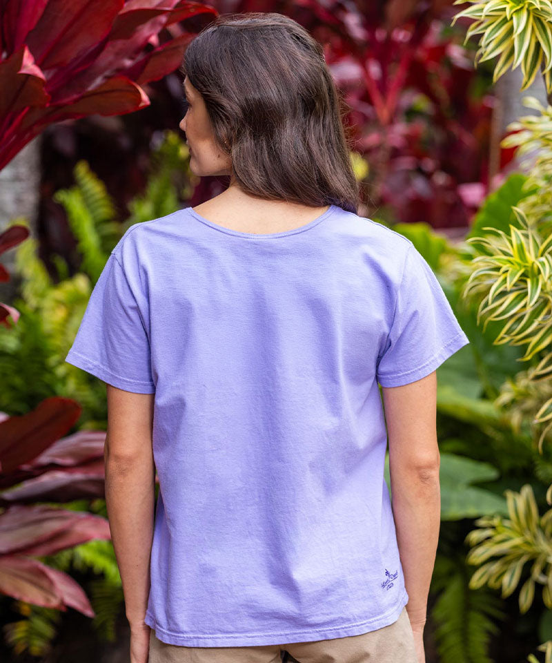 Person wearing a purple t-shirt standing among tropical plants View 3