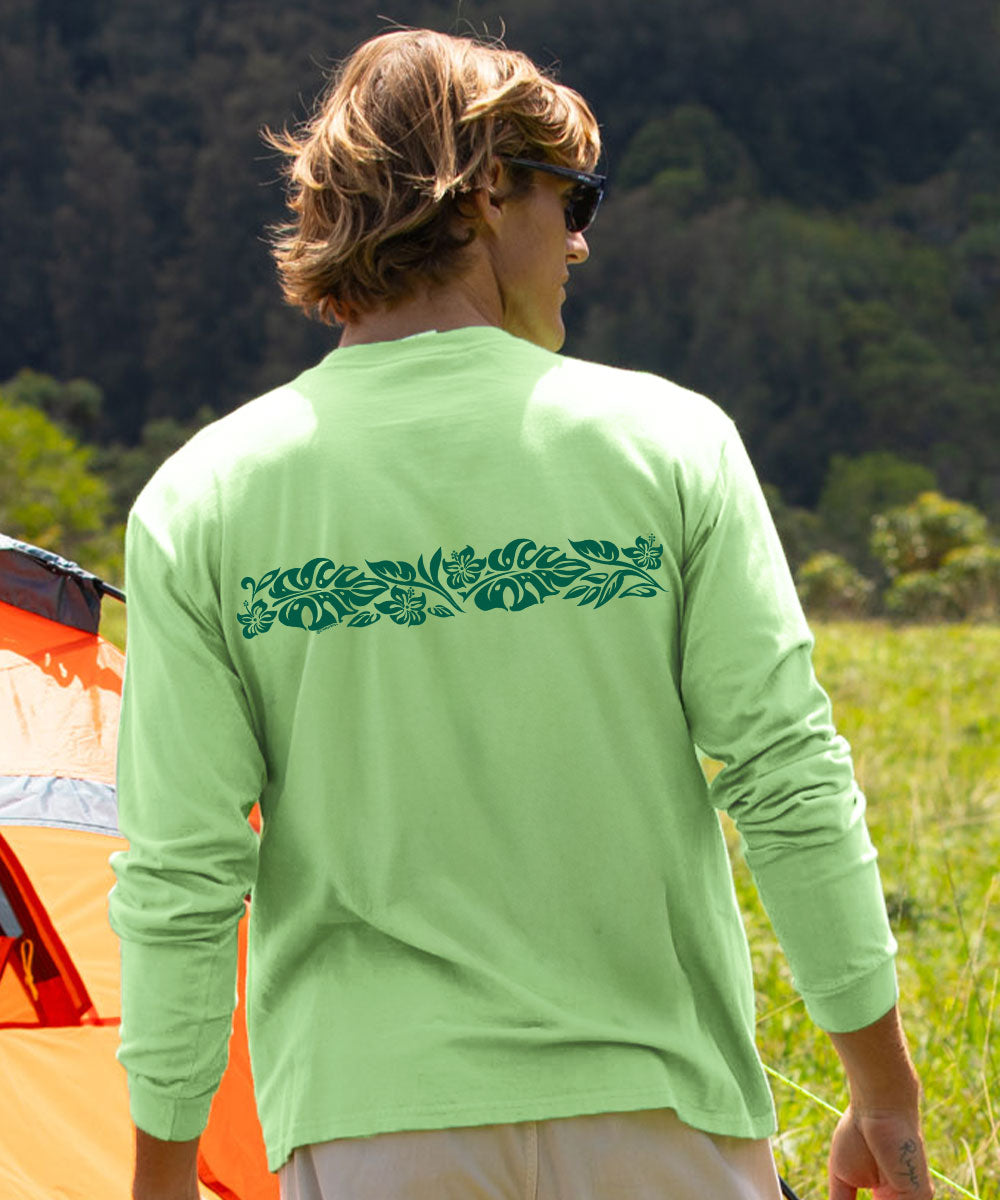 A man viewed from behind wearing a light green long-sleeve shirt with a dark green tropical leaf pattern across the upper back, standing outdoors in a grassy field with a tent and forest in the background. View 3