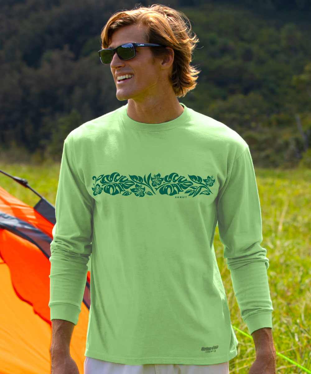 A man wearing a light green long-sleeve shirt with a dark green tropical leaf pattern across the chest, standing outdoors in a grassy field with a tent and trees in the background. View 2