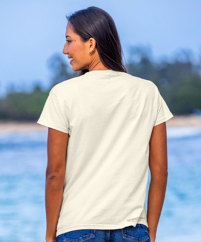 Woman wearing a white t-shirt and blue jeans standing by a body of water with trees in the background. View 3