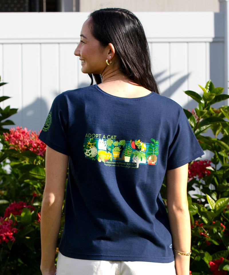 Person wearing a navy blue t-shirt with a graphic and text, standing outdoors with plants and flowers in the background. View 3