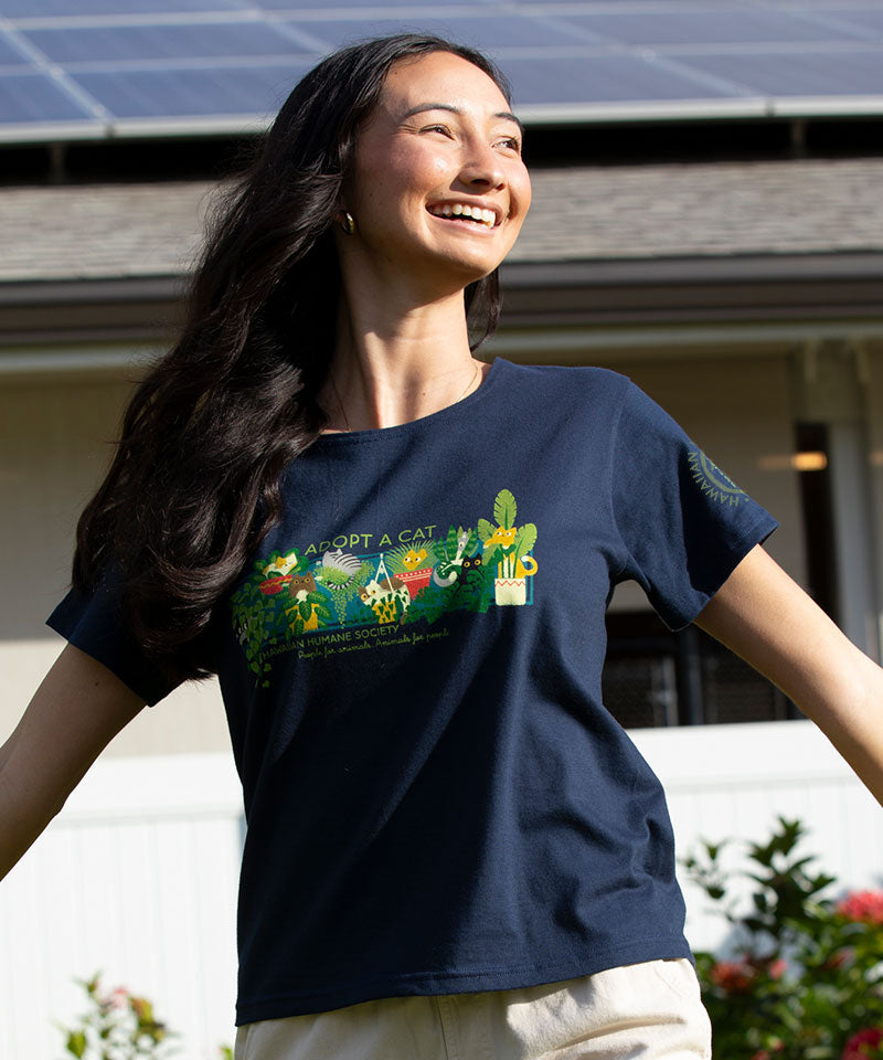 Woman wearing a navy blue t-shirt with a colorful graphic and text, standing outdoors. View 2