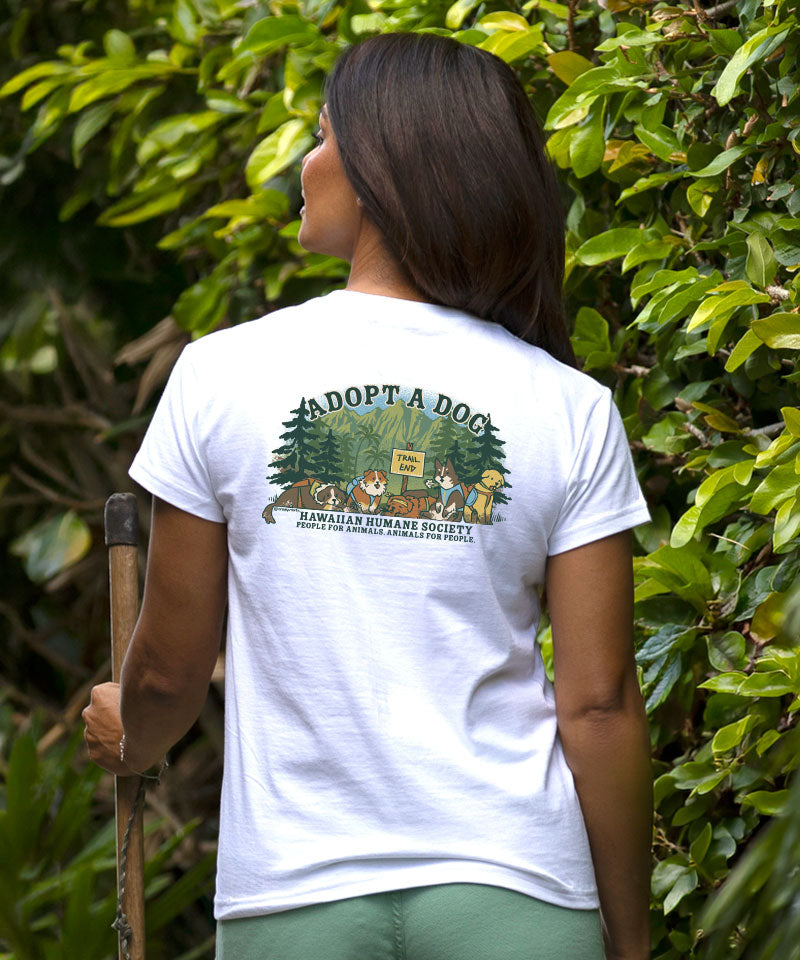 Person wearing a white t-shirt with a graphic and text, standing in front of green foliage. View 3