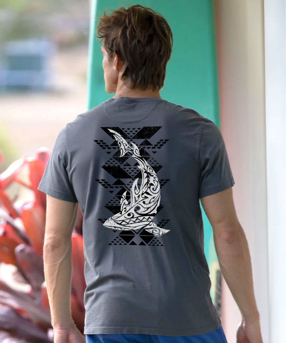 A man viewed from behind wearing a dark gray t-shirt with a large white tribal fish graphic and black geometric patterns on the back, set against a blurred background. View 2