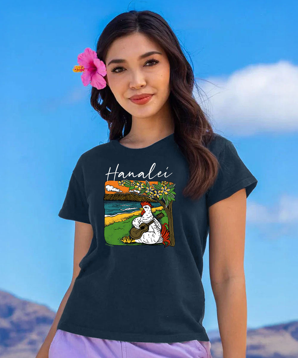 A woman wearing a dark charcoal gray t-shirt with a colorful graphic print of a Hawaiian woman and the word 'Hanalei' in white script, set against a blue sky background. View 2