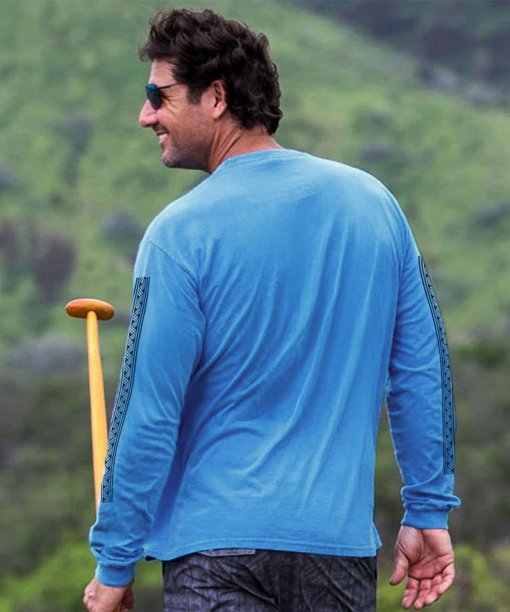 A man wearing a bright blue long-sleeve shirt with dark patterned sleeve stripes, photographed outdoors against a blurred green hillside background. View 3