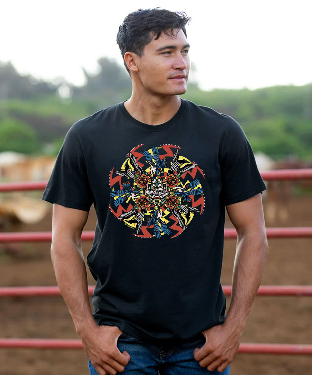 A man wearing a black short-sleeve t-shirt with a colorful circular graphic print on the chest, standing in front of a blurred outdoor background with red railings. View 2