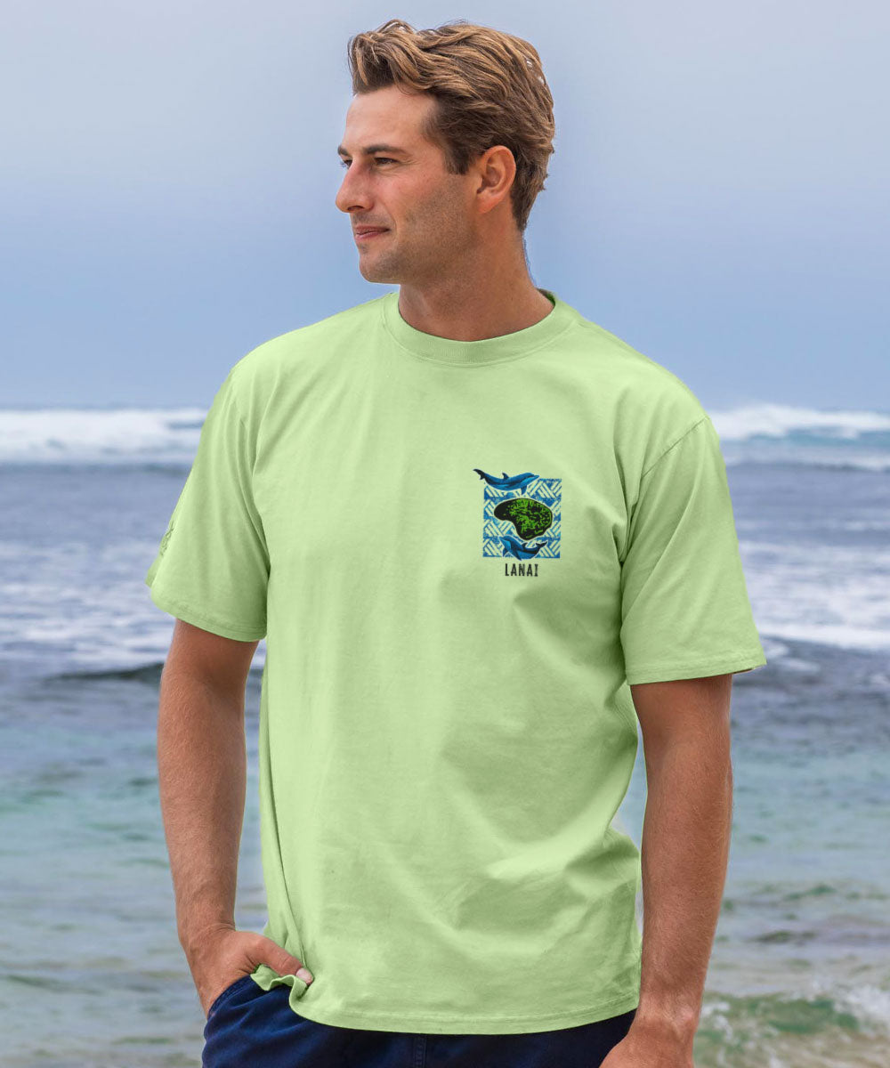 Man wearing a light green t-shirt with a graphic design standing on a beach. View 3