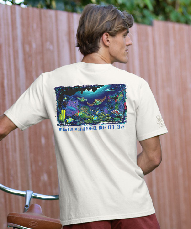 Person wearing a white t-shirt with a colorful graphic and text on the back, standing against a wooden fence.