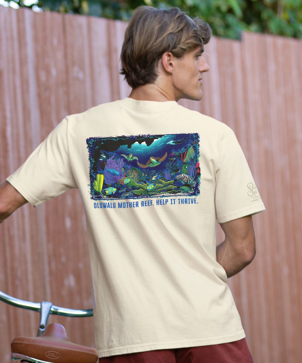 Person wearing a white t-shirt with a colorful graphic and text on the back, standing against a wooden fence. View 2