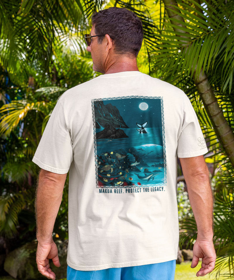 Man wearing a white t-shirt with an ocean-themed graphic and text, standing in a tropical setting.
