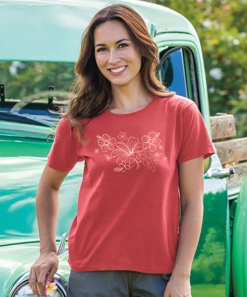 A woman wearing a coral red short-sleeve t-shirt with a white floral graphic on the front, standing in front of a vintage green truck. View 2