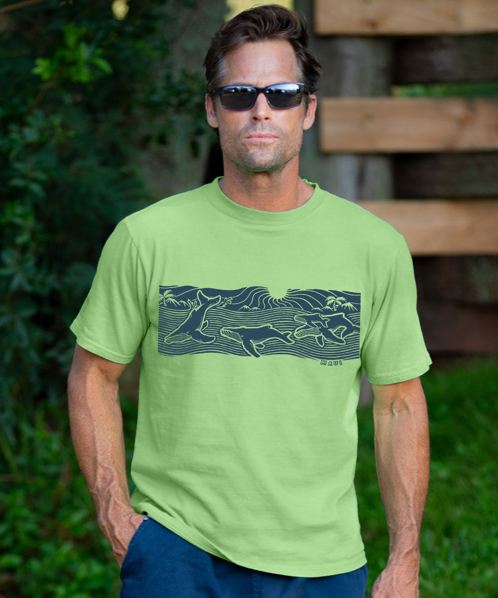 A man wearing a lime green crewneck t-shirt with a dark navy blue graphic of running deer, photographed outdoors against a blurred background of green foliage and wooden planks. View 2