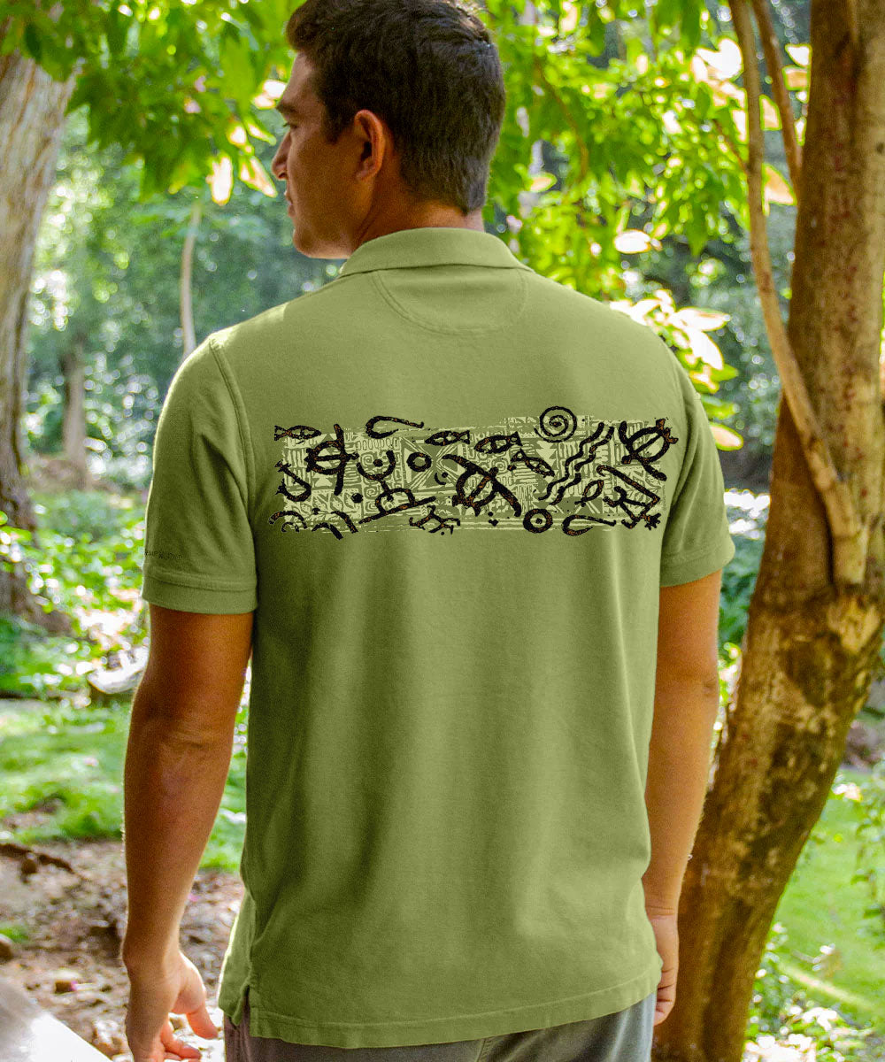A man viewed from behind wearing an olive green polo shirt with a black abstract graphic print across the upper back, set against a lush green outdoor background. View 3