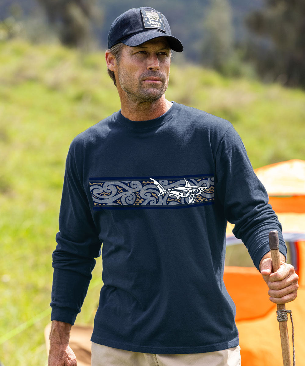 A man wearing a navy blue long-sleeve shirt with a horizontal tribal-style graphic band across the chest, paired with a matching navy baseball cap and khaki pants, standing outdoors in a grassy field. View 2